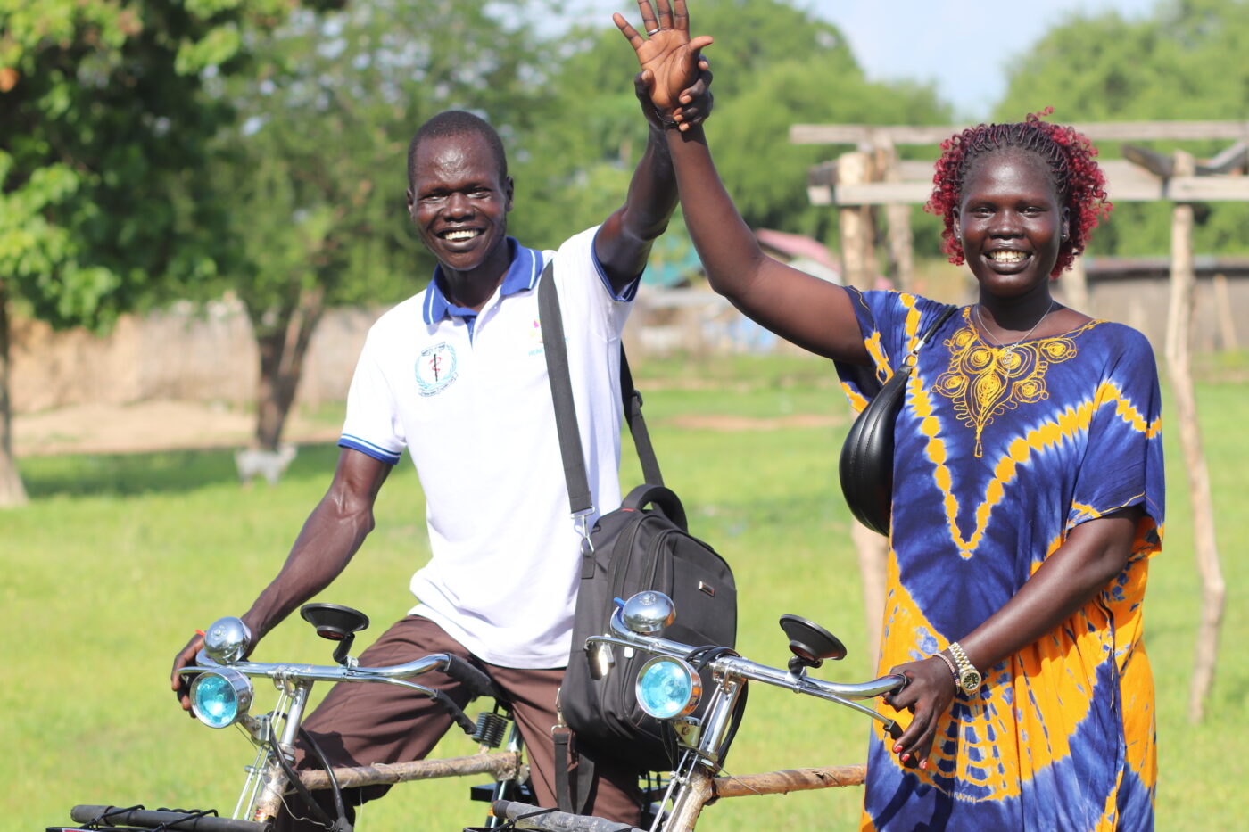 South Sudanese man and woman on a bike holding their hands up while smiling and looking at the camera