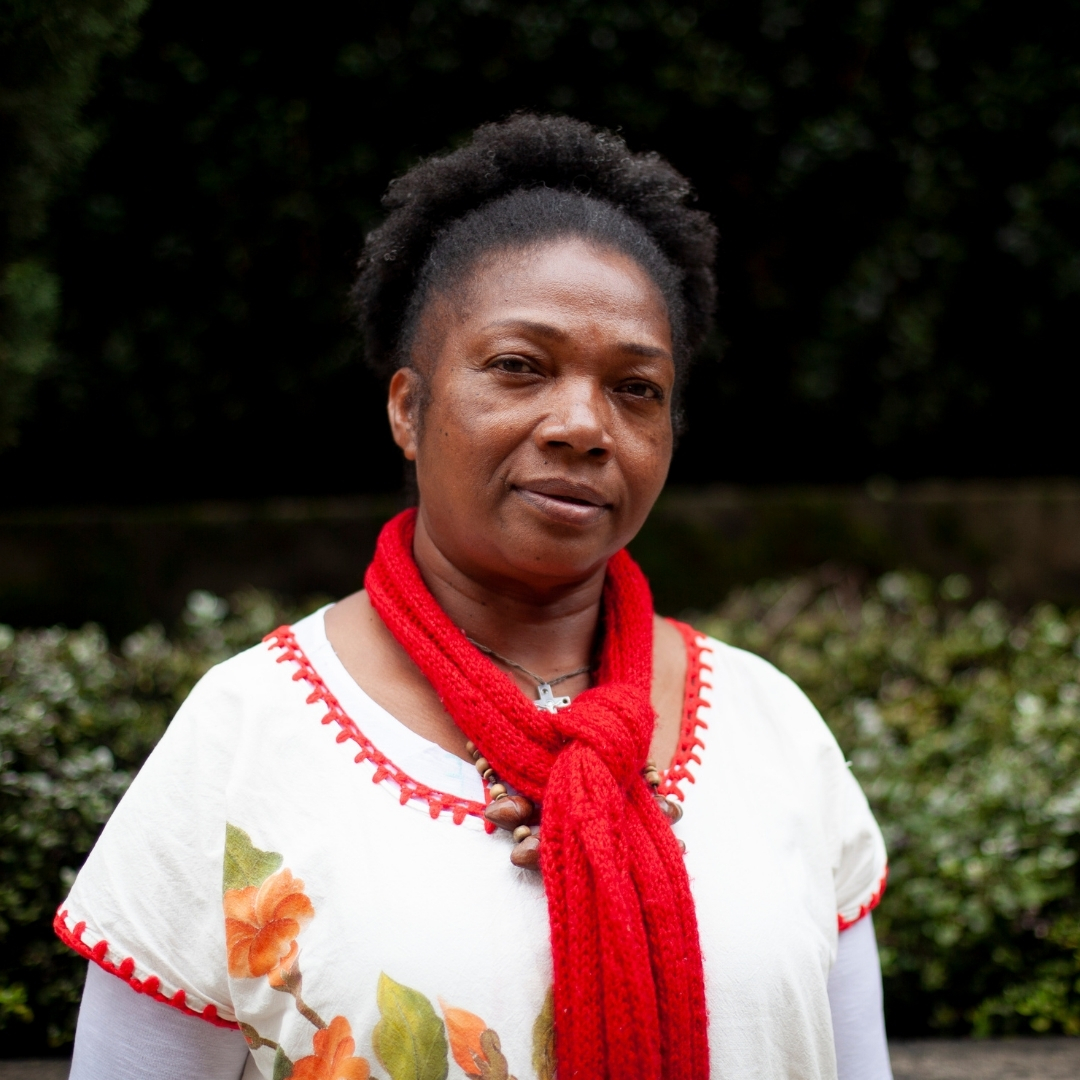 An afro Colombian woman with white clothing and a red scarf looks at the camera