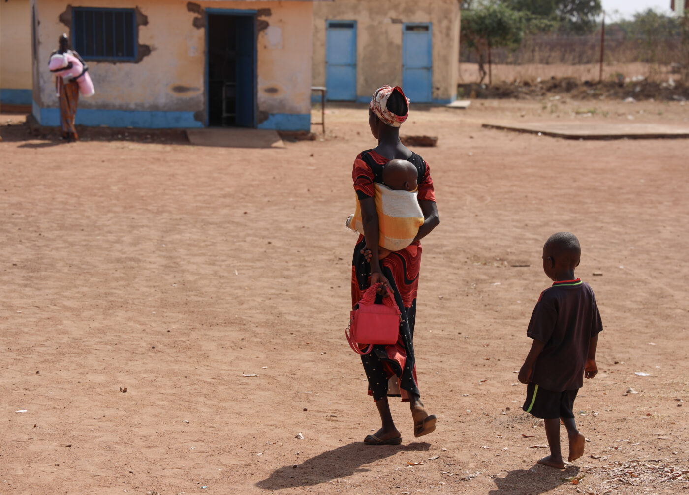 A South Sudanese woman walking with her two little children towards a health facility