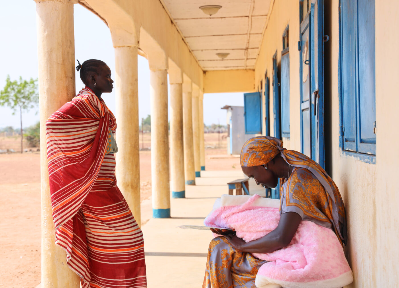 Two women, one of them holding a newborn, outside health facility in South Sudan