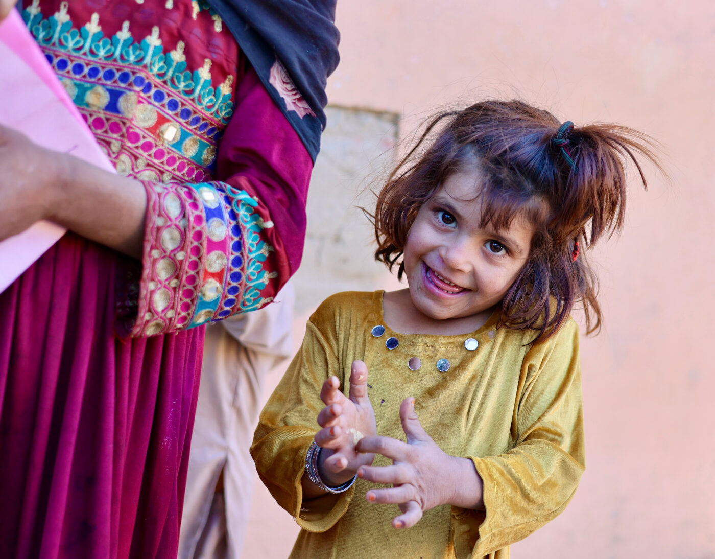 Little Afghan girl smiles next to woman with colorful clothes