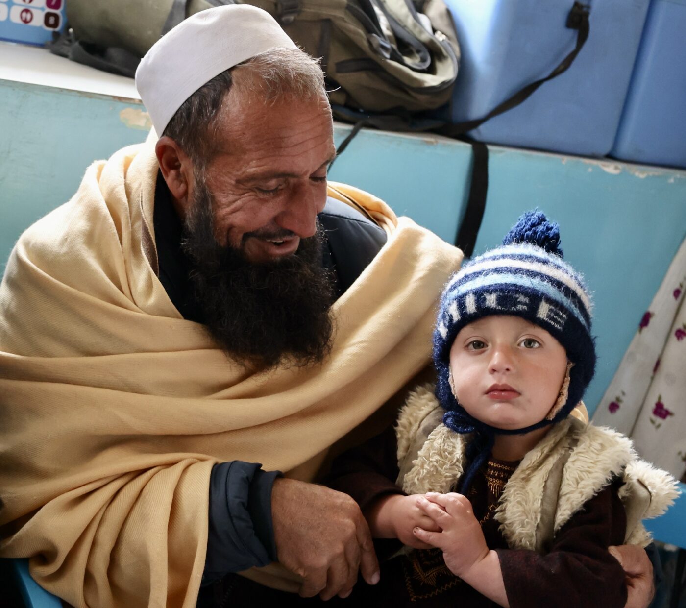 Afghan man sits on a hospital waiting room with a young boy on his lap