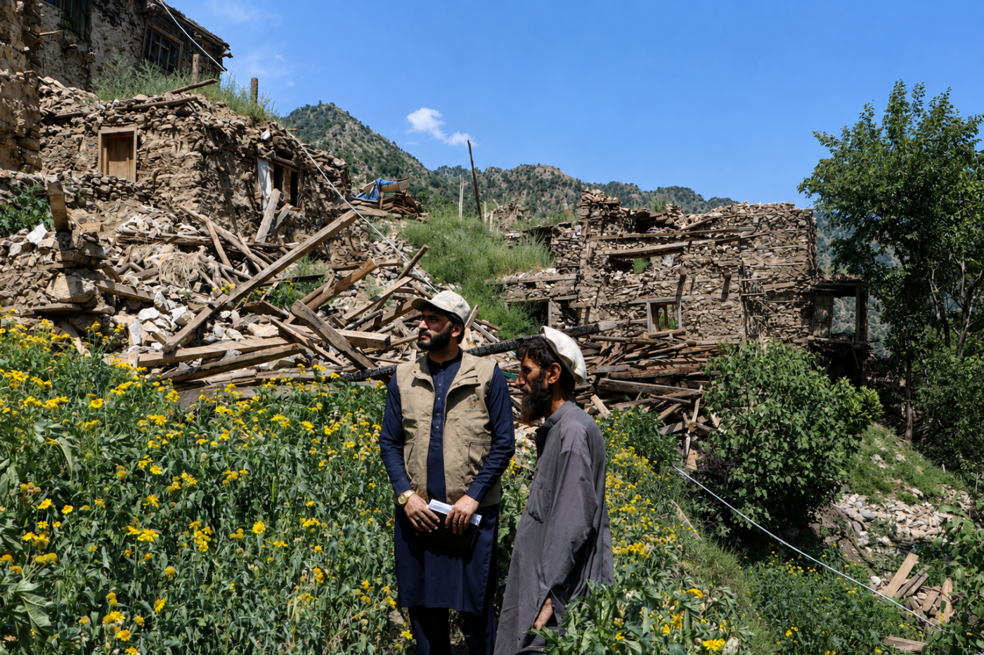 Two men stand among damaged stone houses and rubble in Arrit Valley, Kunar, Afghanistan.