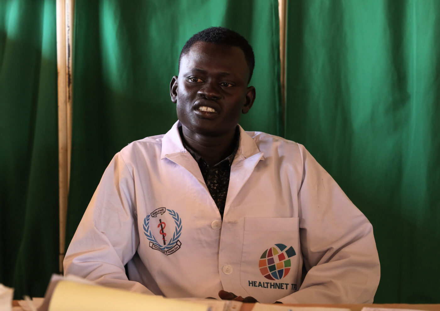 A doctor in South Sudan sits behind a desk and looks at the camera